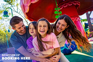 A smiling family of four hugging in front of a theme park ride.
