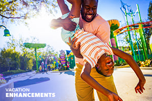 A smiling father holding his laughing son upside down in front of a rollercoaster.